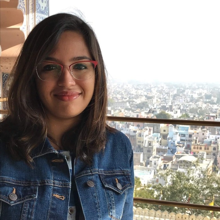 Headshot of Ankita Chakrabarti wearing a denim jacket and red glasses